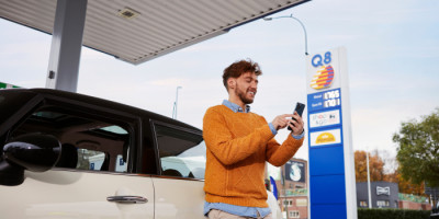 Een man in een oranje trui die met zijn gsm aan het betalen is via de Q8 app.